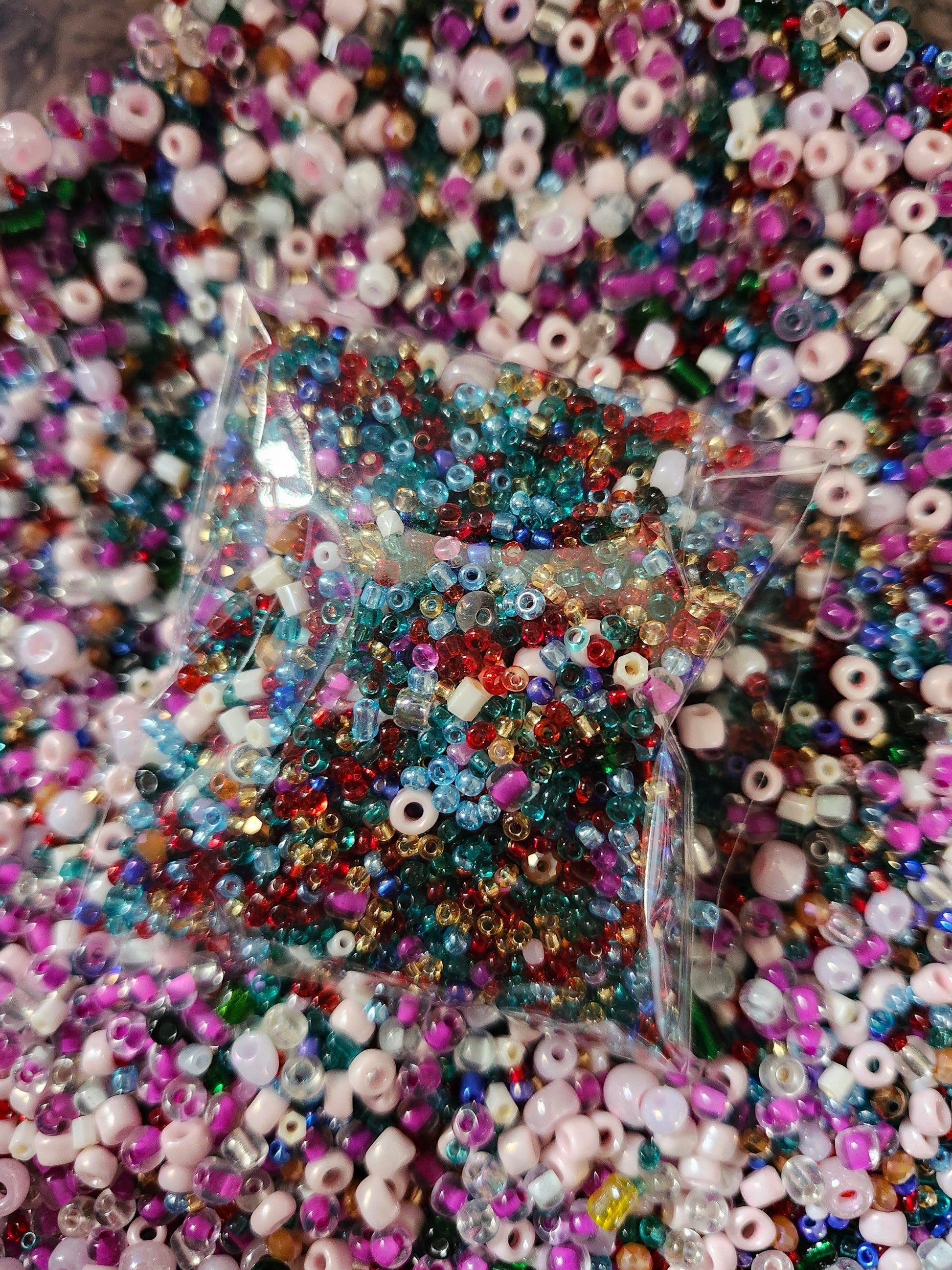Colorful glass seed beads in a clear bag, surrounded by a colorful assortment of beads
