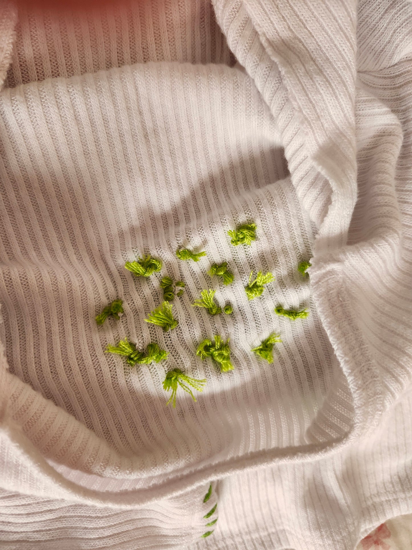 Close-up of handsewn embroidered frog shirt showcasing vibrant green embroidery details on a white fabric