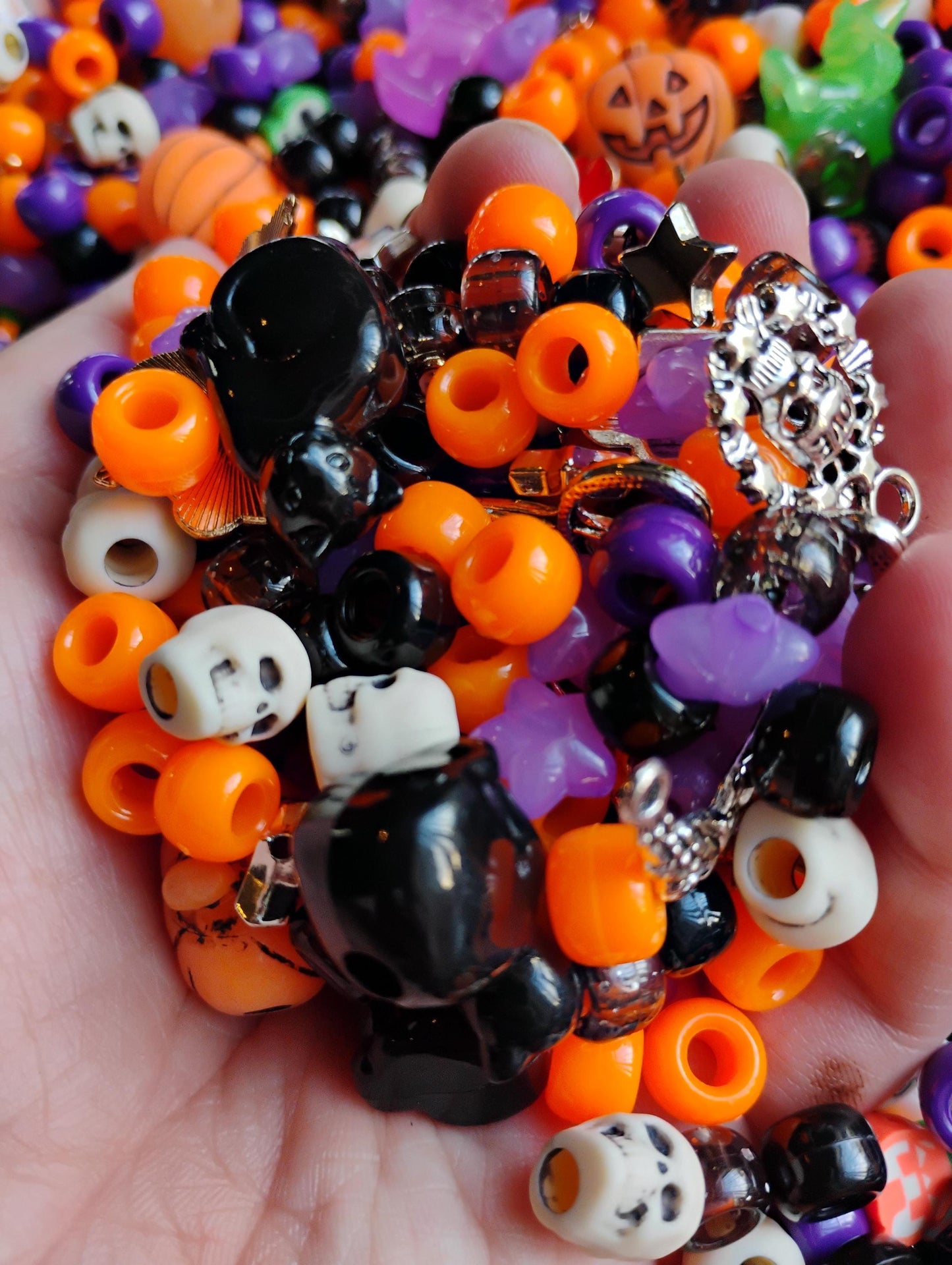 A vibrant mix of Kandi beads Halloween featuring orange, purple, black, and spooky designs in a hand