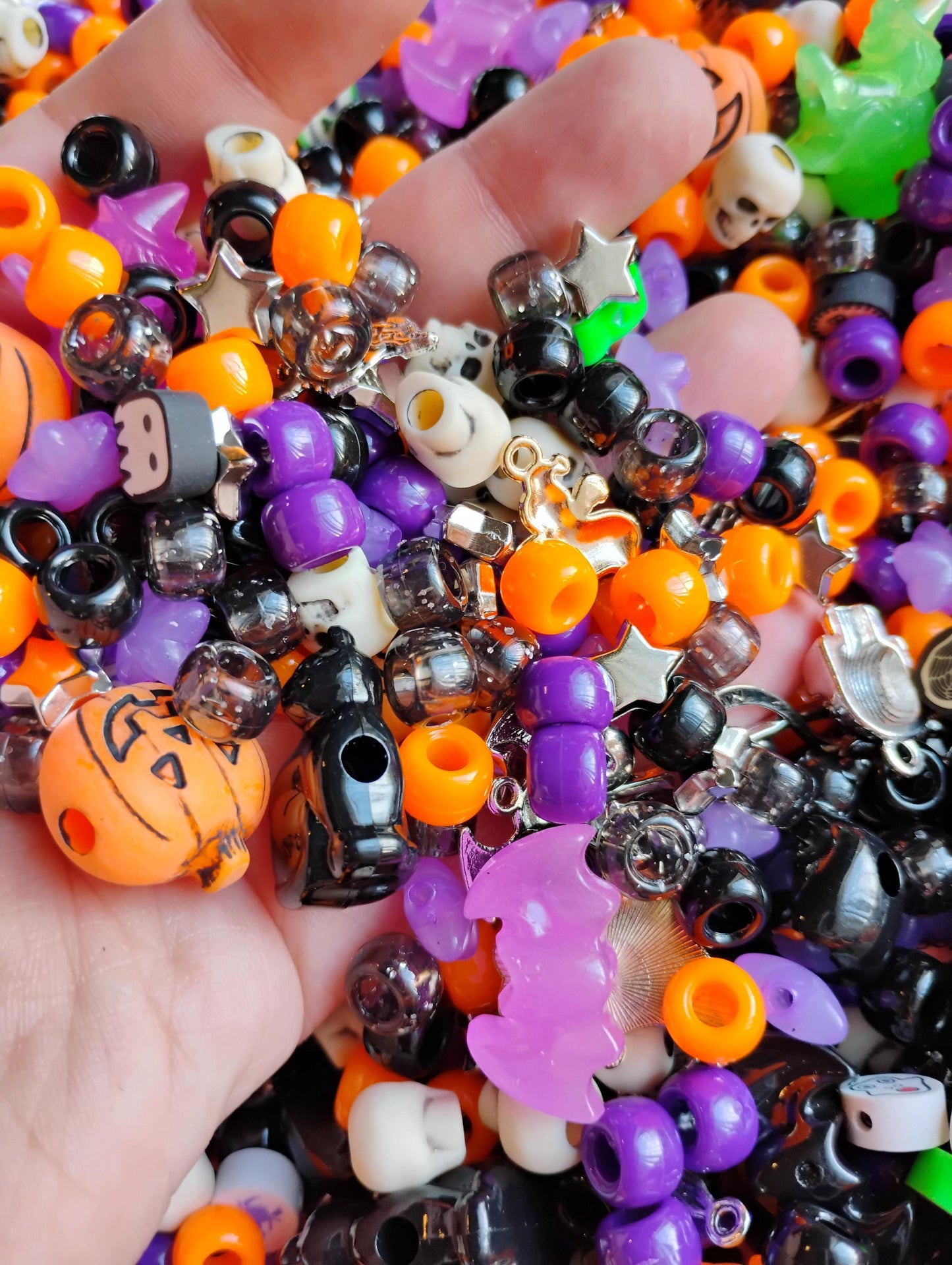 A hand holding a colorful mix of Kandi beads Halloween in vibrant orange, purple, black, and green