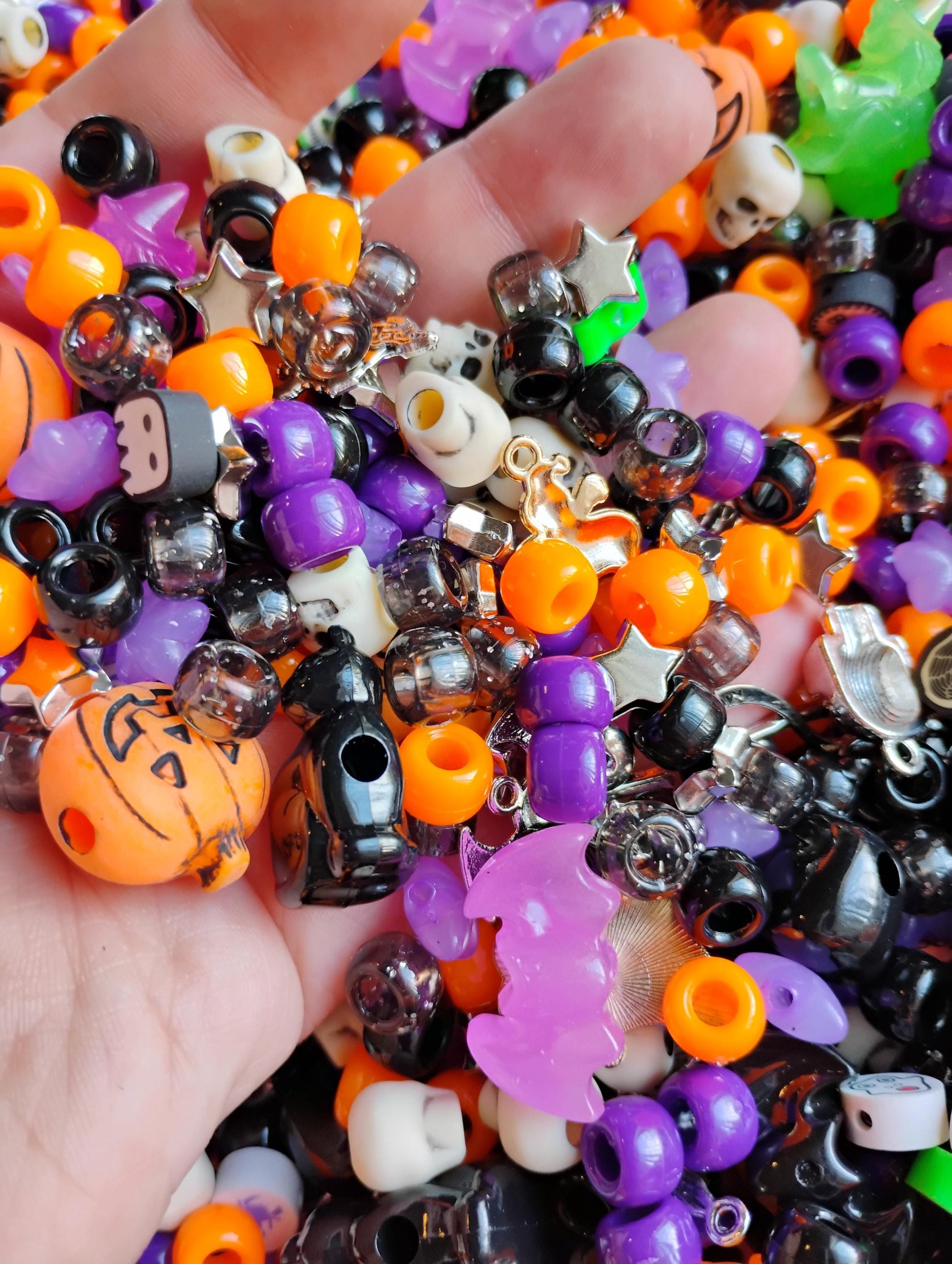 A hand holding a colorful mix of Kandi beads Halloween in vibrant orange, purple, black, and green