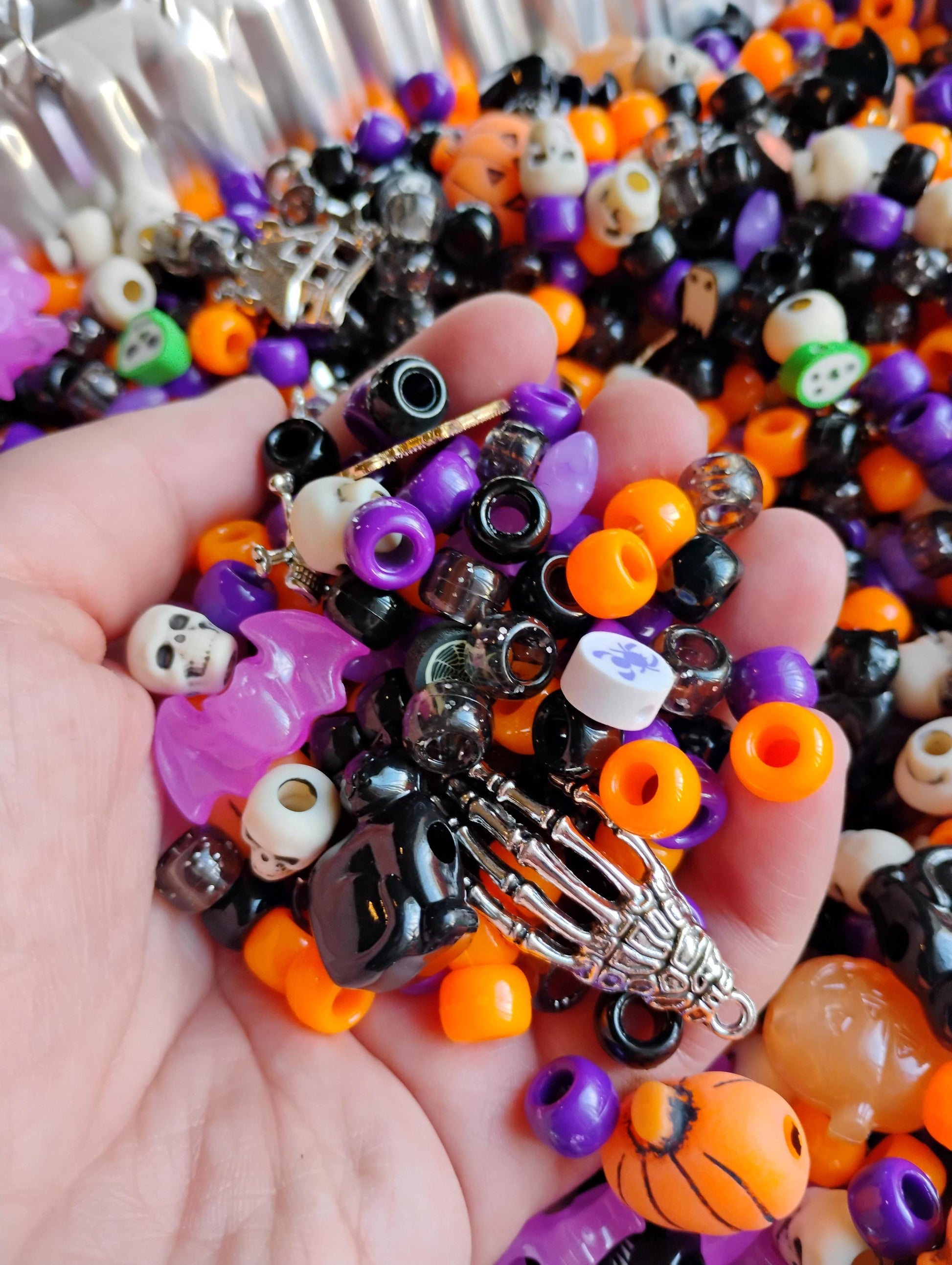 Hand holding assorted Kandi beads Halloween in vibrant colors with skull and skeleton charms