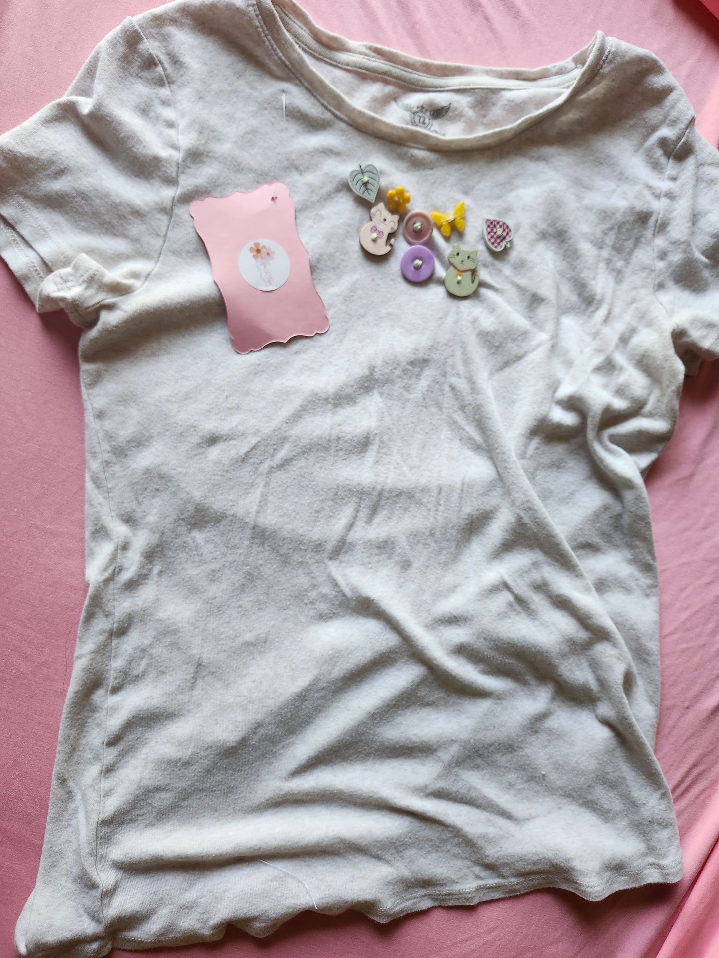 White T-shirt featuring quirky button designs on the chest in playful colors and shapes
