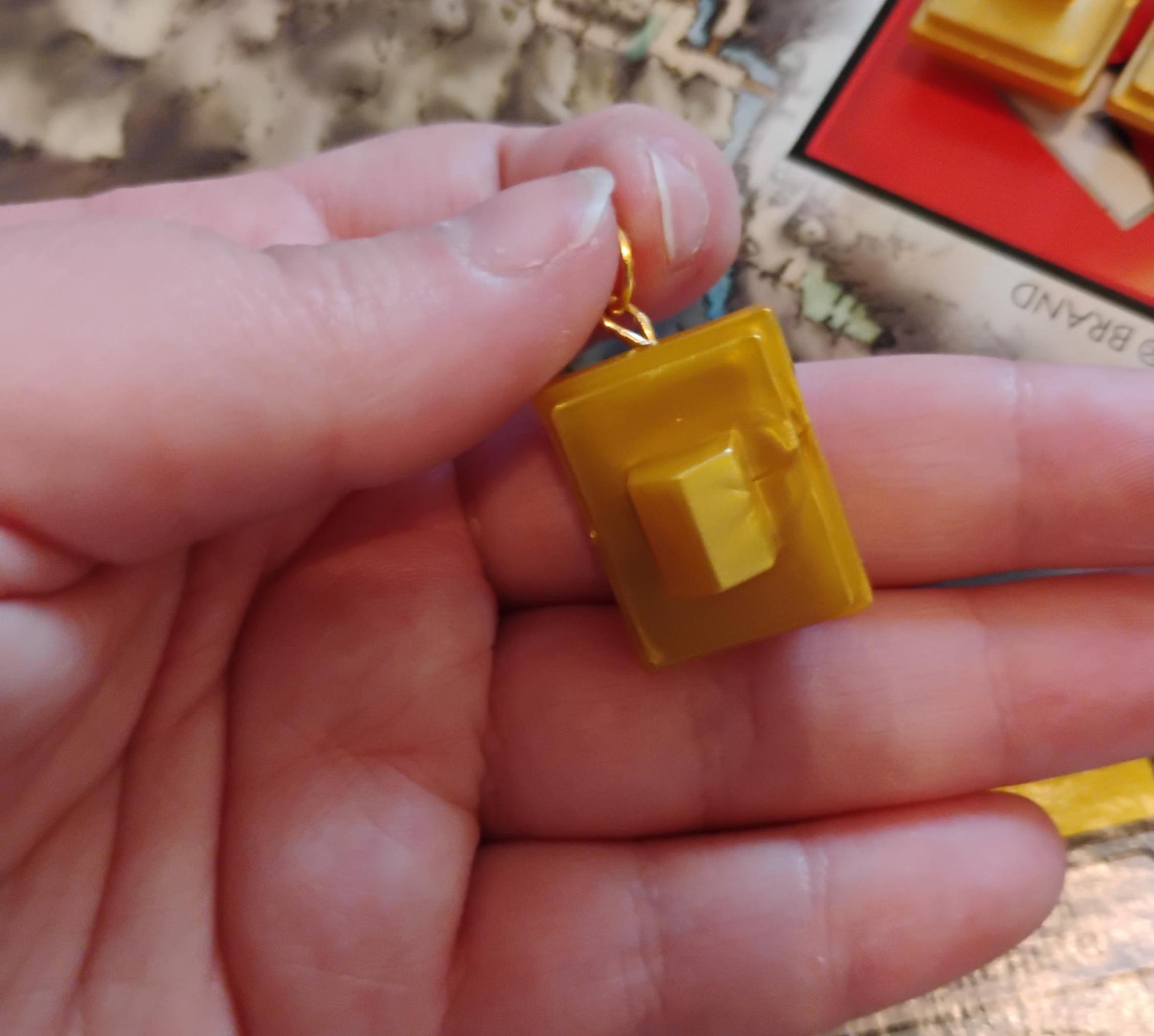 Hand holding a yellow resin block charm with a gold clasp from FlowersForFaye